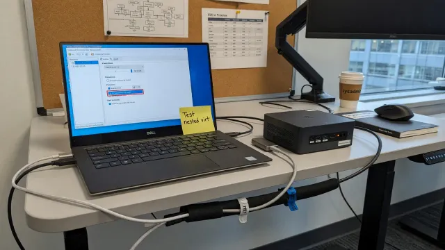 Laptop virtualization settings next to a compact mini-PC on a standing desk