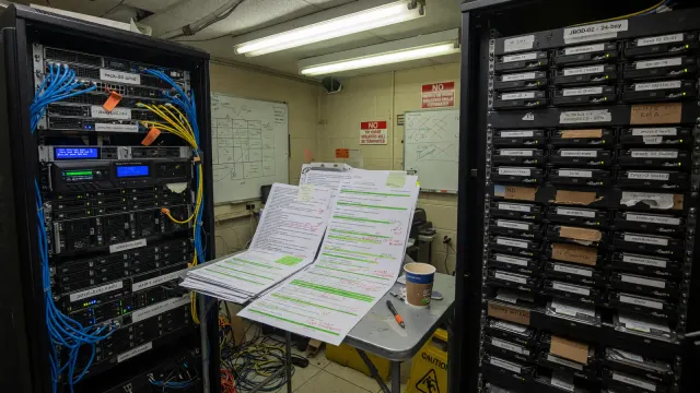 Rack-mounted server beside stacked log printouts and a crowded disk shelf