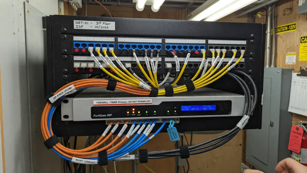 Network closet with ethernet patch panel, labeled cables, and a small firewall appliance
